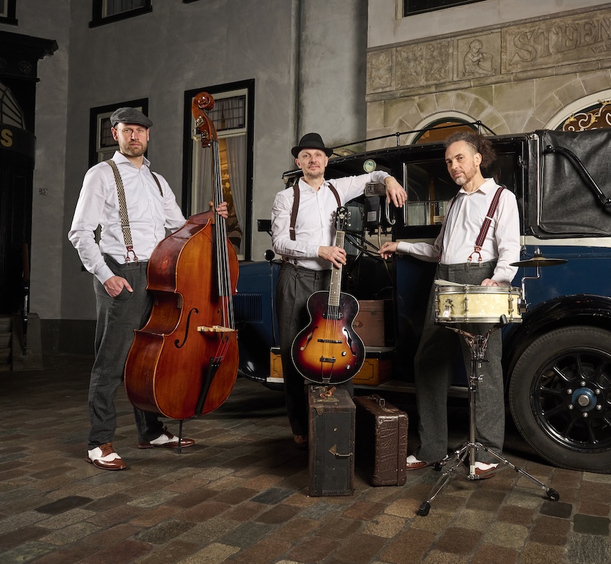 Akoestisch trio Moon About met contrabas, gitaar en snaredrum bij een oude auto